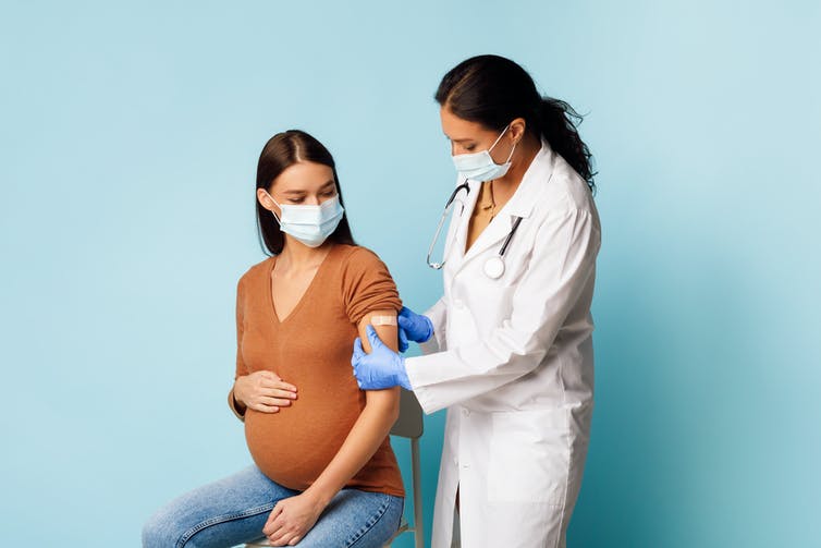 Un travailleur de la santé appose un bandage sur le bras d’une femme enceinte après son vaccin